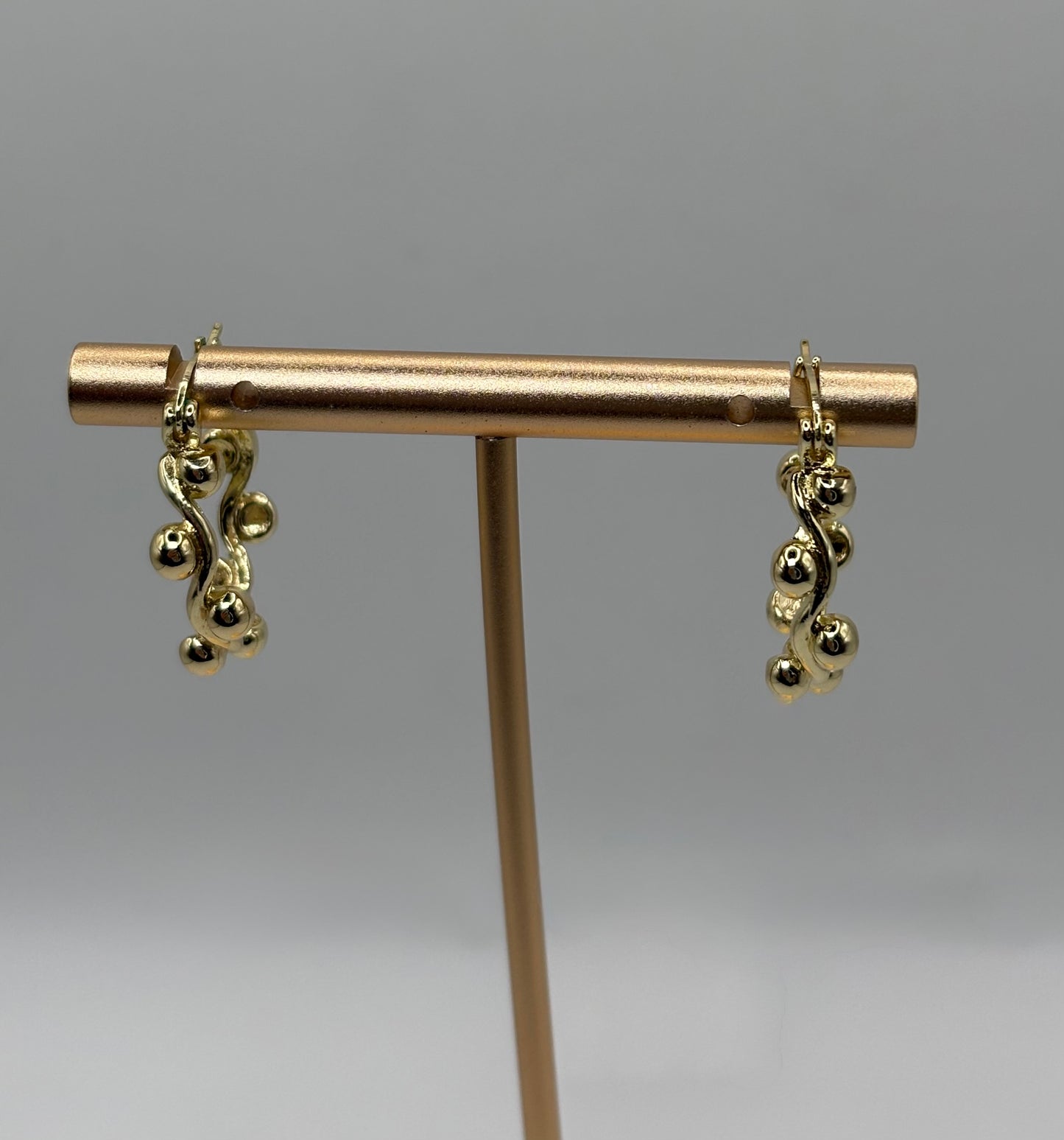 These elegant gold drop earrings feature a captivating organic design that mimics twisting vines or gentle waves, adorned with clusters of smooth, polished gold spheres.