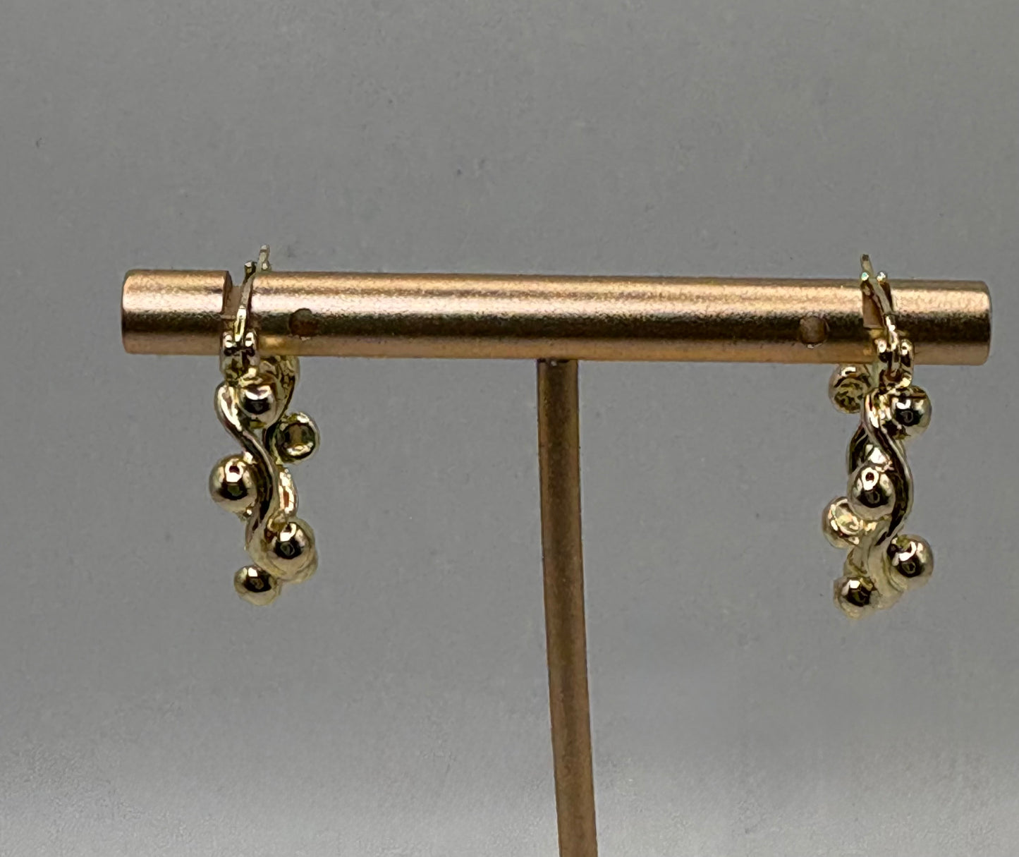 These elegant gold drop earrings feature a captivating organic design that mimics twisting vines or gentle waves, adorned with clusters of smooth, polished gold spheres.
